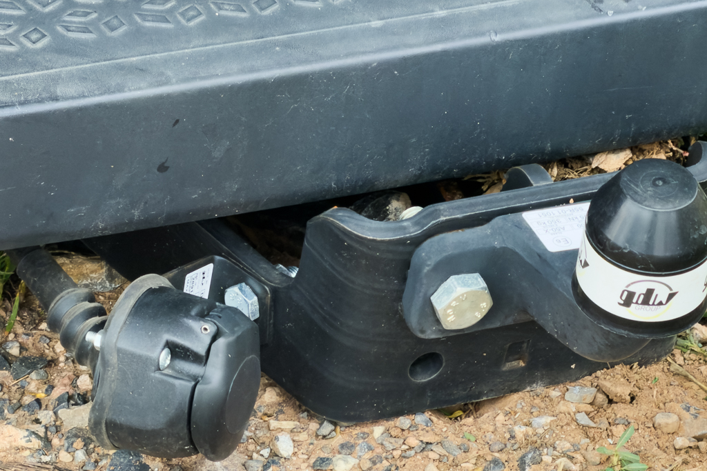 Close-up view of a trailer hitch assembly showing connection points and hardware on a gravel surface.