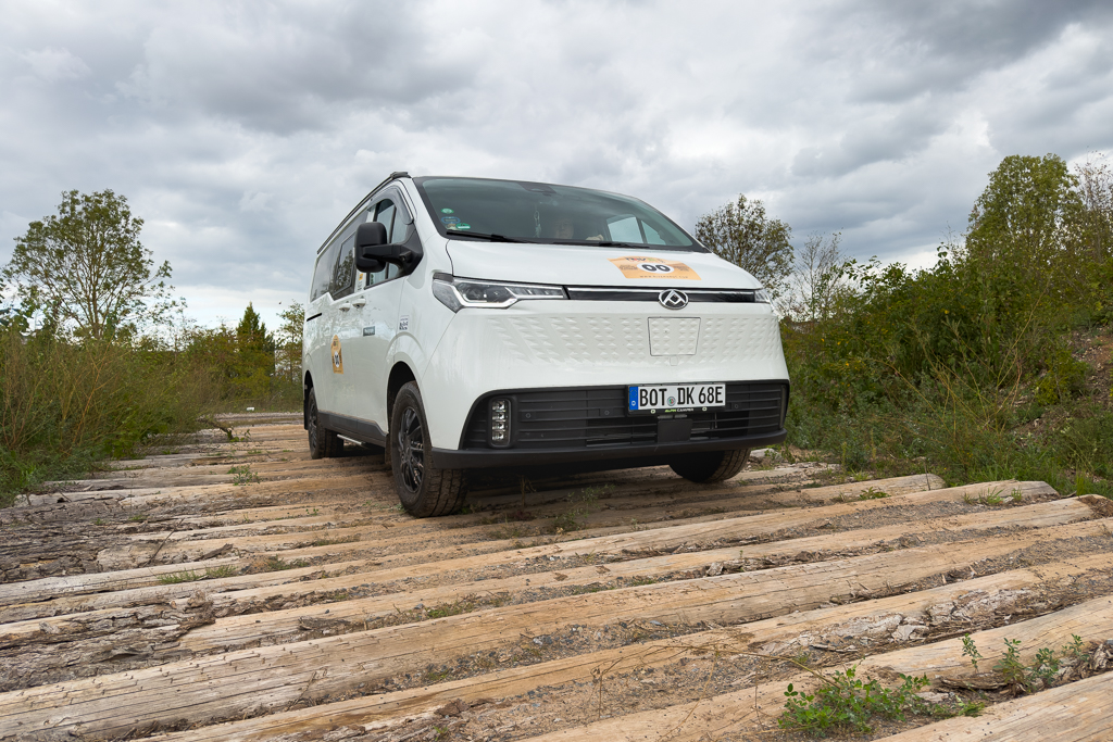 A white van parked on wooden planks in a grassy area, under a cloudy sky.