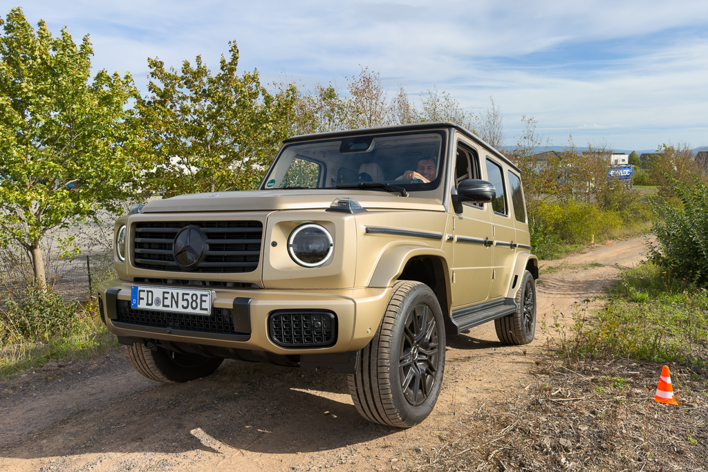 A beige Mercedes-Benz G-Class SUV parked on an off-road track surrounded by greenery.
