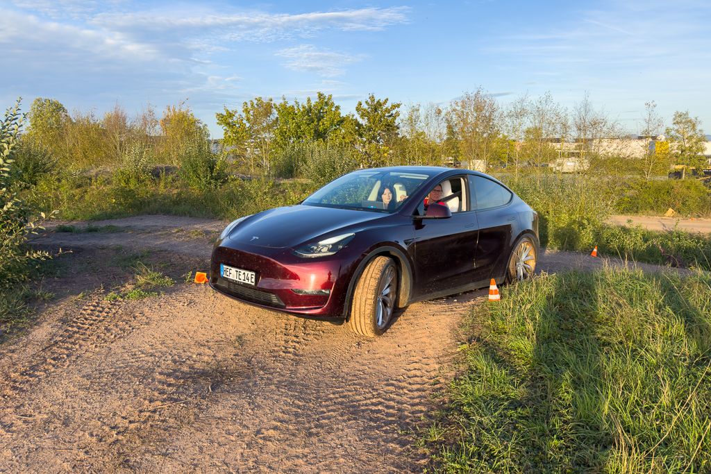 A dark red electric SUV navigating a dirt trail with greenery in the background, featuring traffic cones positioned along the path.