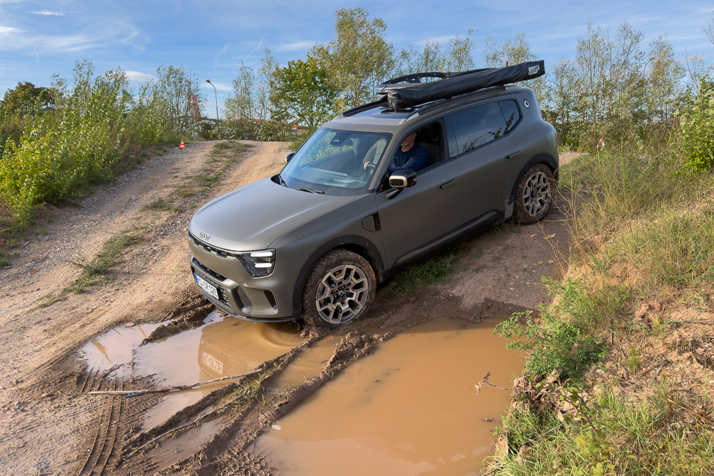 A rugged SUV maneuvering through a muddy off-road path with a driver visible inside.