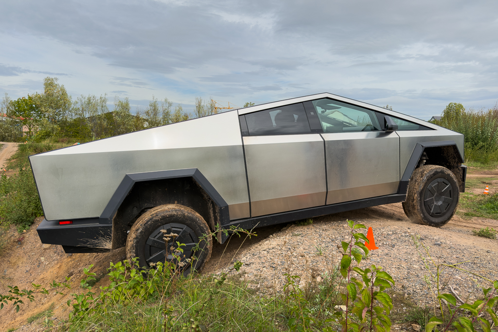 A Tesla Cybertruck navigating an off-road terrain, showcasing its unique angular design and metallic finish.