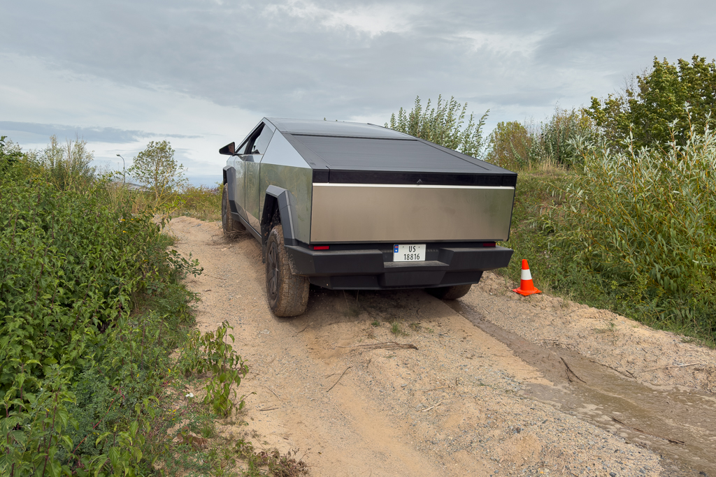 A futuristic electric truck navigating a dirt path surrounded by greenery, with a traffic cone nearby.