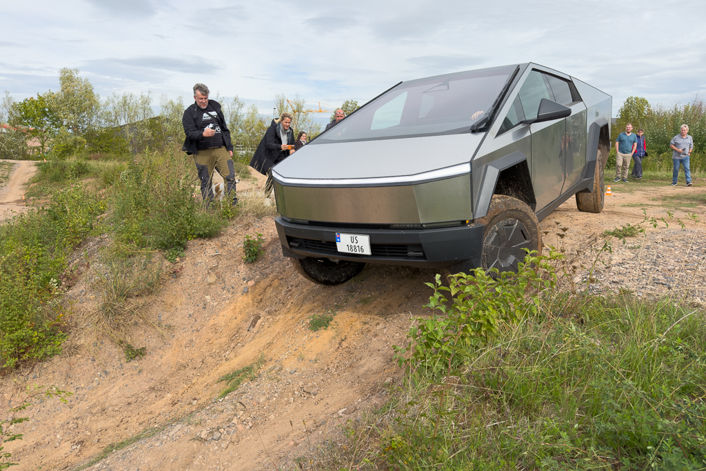 A futuristic electric pickup truck navigating a rugged dirt terrain, surrounded by onlookers observing the demonstration.
